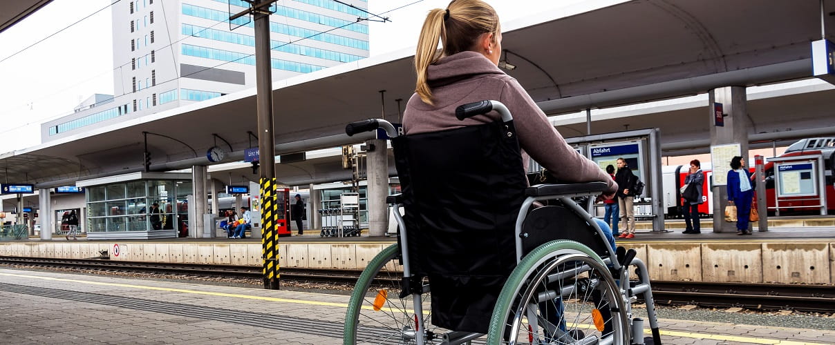 Frau sitzt in einem Rollstuhl auf einem Bahnhof