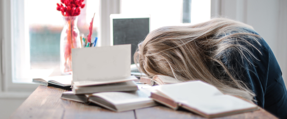 Person gelangweilt über einem Stapel Bücher sitzend