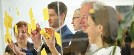 Menschen kleben Post-it-Zettel an Glaswand Menschen kleben Post-it-Zettel an Glaswand