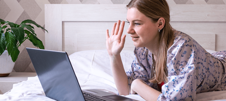 Frau am Laptop auf Bett winkt