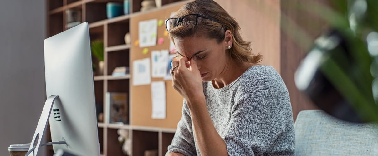 Frau vor PC greift sich an die Stirn Burnout macht sich lange vor dem eigentlichen Arbeitsausfall bemerkbar und ist nicht das Problem einzelner Individuen
