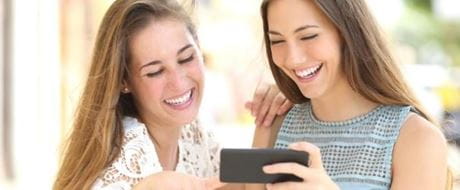 Lachende Frauen schauen zusammen Medieninhalte auf Smartphone an Lachende Frauen, die sich zusammen Medieninhalte auf Smartphone anschauen