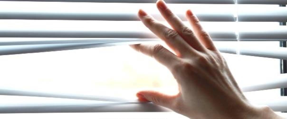 Aufnahme einer Hand, die Lamellen einer Jalousie auseinanderdrueckt