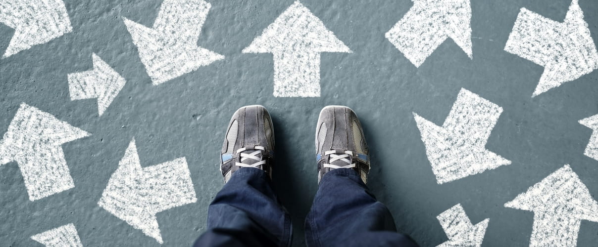 Schuhe und Pfeile auf Asphalt Wie soll ich mich in einer unbekannten, verwirrenden Situation entscheiden